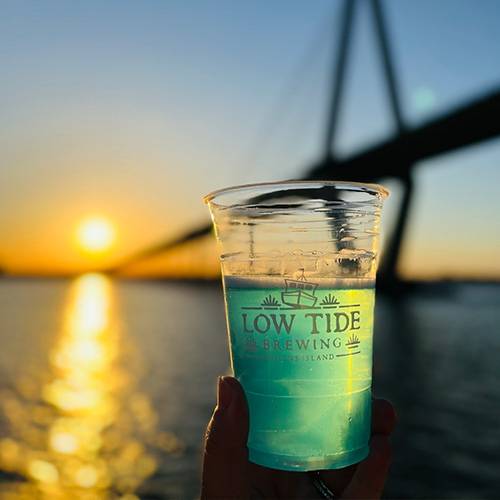 low tide brewing glass with teal drink held in front of sunset